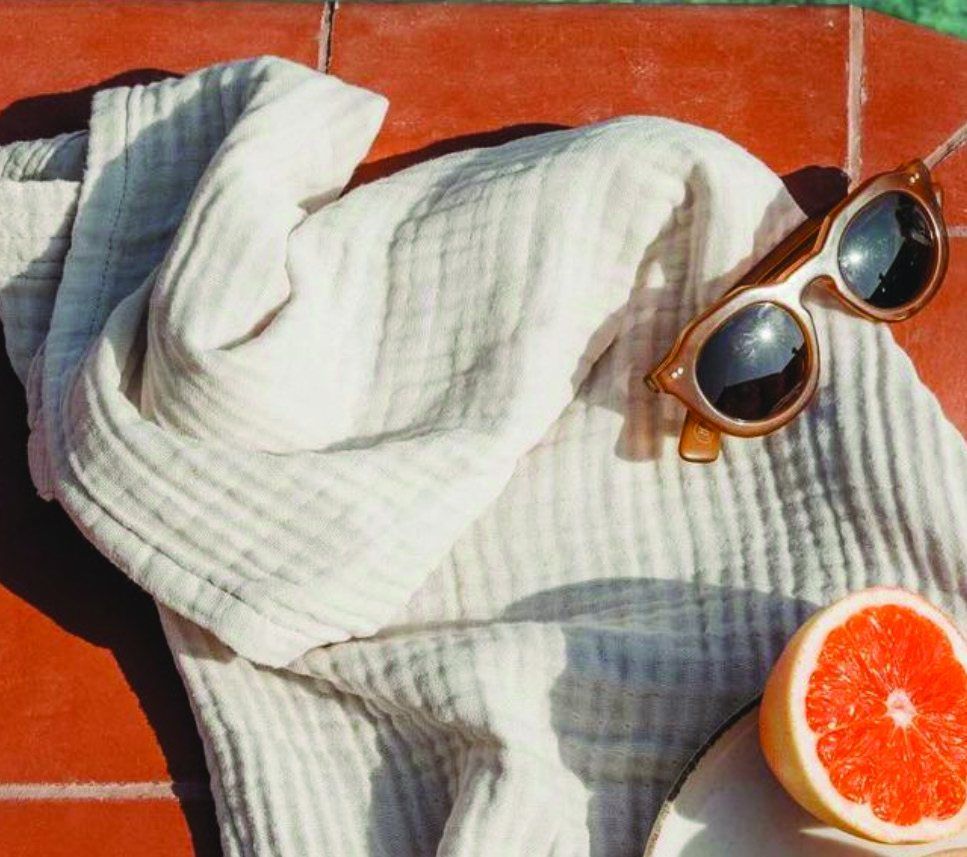 A folded towel, sunglasses and a halved grapefruit on terracotta tile