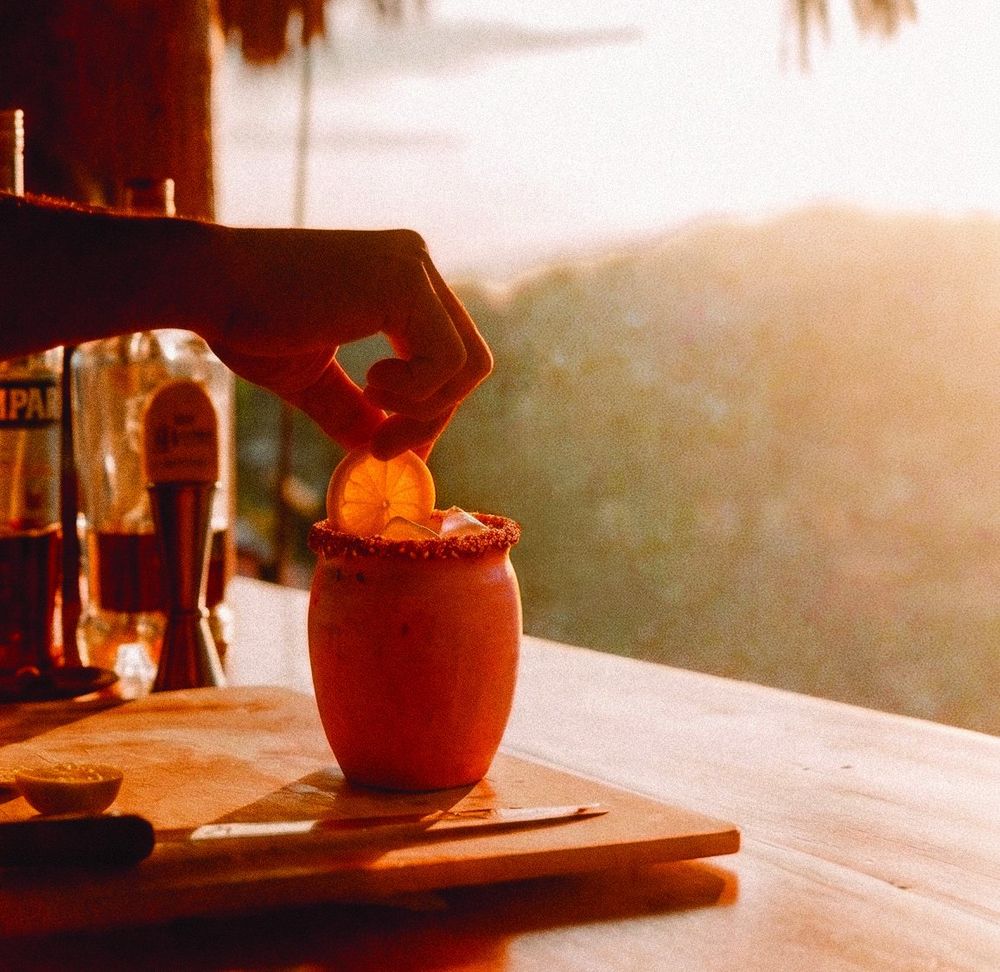 A bartender pouring a drink into a clay cántaro cup at golden hour